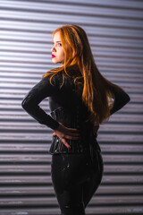 Red-haired girl in latex, a black top and tight pants, on a metal background, posed on her back