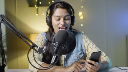 Young Indian girl vlogger live recording or streaming and checking likes, comments or chatting on social media with channel subscribers on mobile phone