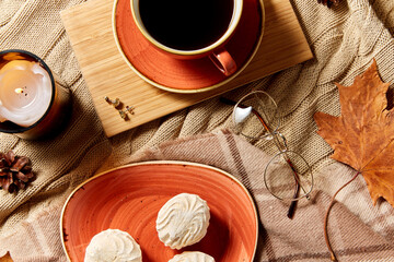 people, season and leisure concept - cup of coffee, autumn leaves, meringues and candle on warm blankets at home