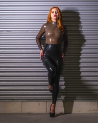 Red-haired girl with latex, tight brown and black suit, posed looking at camera, vertical photo