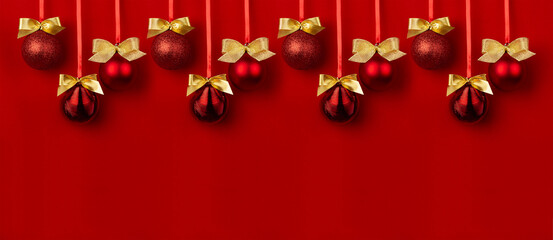 Pattern of balls with gold bows hanging on ribbon in row on deep red background, copy space, border. Luxury fashion christmas banner for design of website, header, poster, flyer, card, brochure.