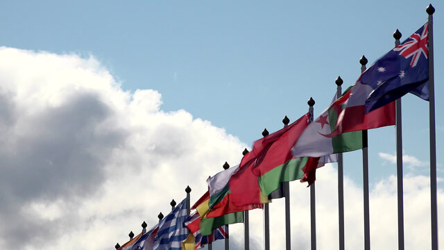 Various world flags flying on flagpoles on background of the sky and clouds