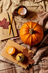 autumn, season and leisure concept - notebook or diary with pencil, pumpkins and candle on warm blankets at home