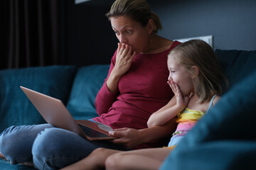 Shocked surprised mom and daughter looking at laptop screen while sitting on couch