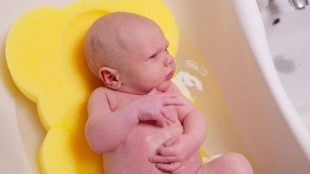 Young mother bathes her newborn baby in a tub of warm water. An adorable boy takes a bath, his mother washes his willy in warm water. Concept is family, mother and son. 