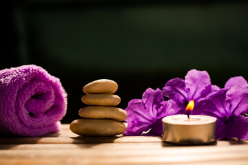 Obraz na płótnie Canvas Light candle with stack zen pebbles stone and towel, flowers on wooden with black background. aroma therapy spa set organic herbal for vacation in holidays. for luxury bathroom hotel concep.