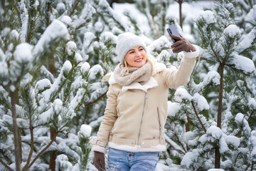 Beautiful woman standing among snowy trees in winter forest and enjoying first snow. Woman in winter woods.