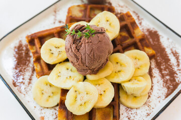 Close-up banana waffles on a white plate with chocolate ice cream and syrup, top view. Healthy breakfast