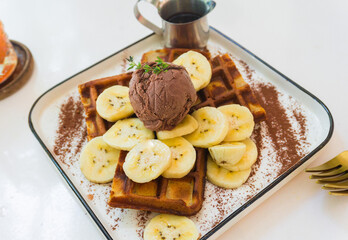 Close-up banana waffles on a white plate with chocolate ice cream and syrup, top view. Healthy breakfast