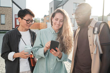 Horizontal medium portrait of three ethnically diverse friends hanging out together watching something in Internet on smartphone