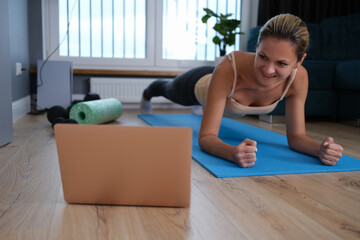 Healthy young woman doing plank exercises at home while watching an online workout session from laptop