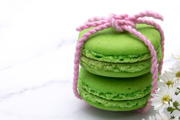 Obraz na płótnie Canvas Closed up of two green macaroons tied with soft pink thread with beautiful tiny white flowers.