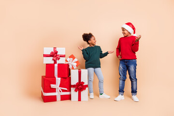 Photo of two friendly kids talk share gifts enjoy tradition wear x-mas hat jumper isolated beige color background