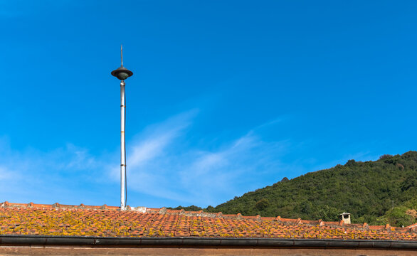 lightning rod on pole. blue sky and forest background. tiled roof