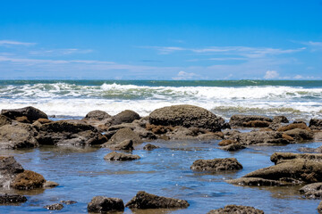 Obraz premium Beautiful rocky stone beach with blue sky and water waves landscape view