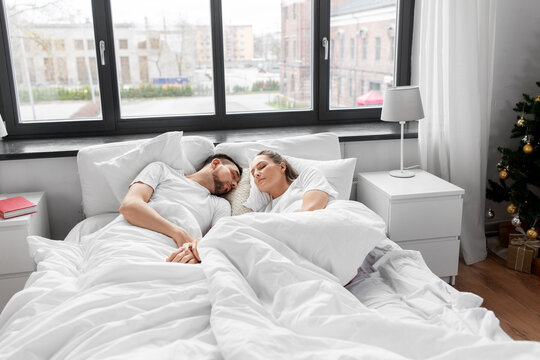 rest, winter holidays and people concept - happy couple sleeping in bed at home on christmas morning