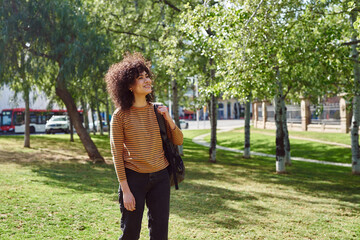 Fototapeta premium Smiling young woman looking at trees in a park
