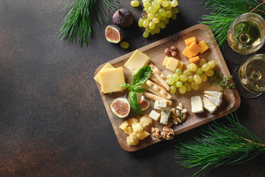 Christmas cheese platter with different cheese and grapes, nuts, olive, figs on a brown background with copy space. Festive holiday appetizer. Xmas brunch.