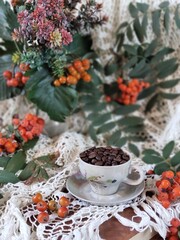 Still life with cup and coffee beans, flowers and rowan on vintage tablecloth