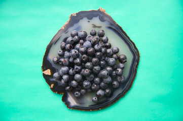 Flat lay of agate gemstone and juicy, fresh blueberries on turquoise table. Isolated sweet bilberry fruits on translucent crystal surface on white background. Copy Space. Healthy raw vegetarian food 