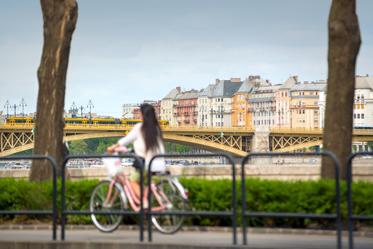 Blurred girl riding bicycle against Margaret bridge and old building of Budapest