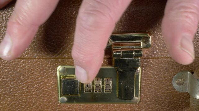 Closeup POV of a man&rsquo;s finger changing the three numbers of a rotary dial combination lock on a case, then using his thumb to move the button to release the case latch.
