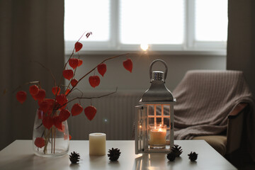 cozy autumn still life, candles, flowers, twigs of orange physalis in a vase and details of home interior