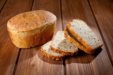 A loaf of delicious white bread made from natural products, on hops with flax saturation, without baker's yeast, on a wooden table surface.