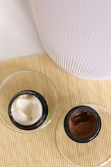 Opened jars of facial cosmetic, white cream and brown mask on wooden table.