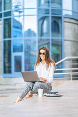 Young business lady working on the laptop outdoors near business center.