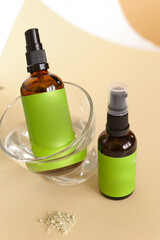 Close up glass spray bottle wirth cosmetic product and green space for brand near leaf.