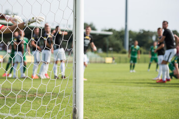 Detail of goal's post with net and football players during free kick in the background.