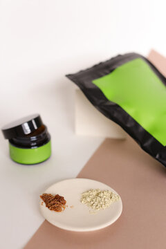Focus on white plate with clay powder near doypack and jar with cosmetic products and green space for brand.