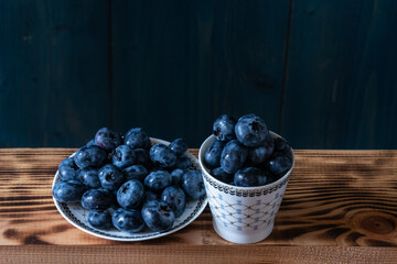 Ripe juicy blueberries in a cup on a wooden table.