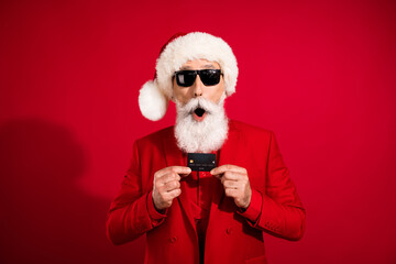 Photo of shocked santa claus hold plastic credit card open mouth wear sunglass x-mas hat suit on red color background