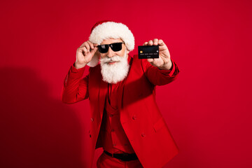 Portrait of elderly pensioner retired cheery bearded grey-haired man showing black bank card sale isolated over bright red color background