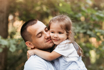 A young father hugs his young daughter in nature. Hugs and kisses