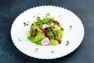 Salad with meat, sun-dried tomatoes and radishes on a plate. Against a dark background.