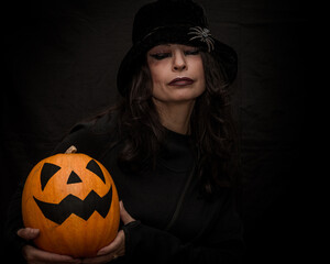 Halloween girl with a pumpkin in her hands on a black background with a spider on her head.