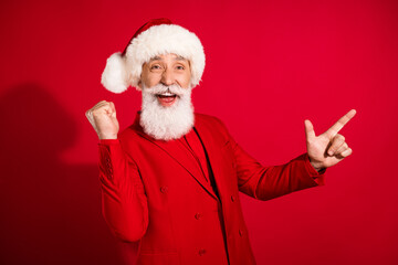 Photo of cheerful winner adviser santa claus direct finger empty space wear x-mas hat suit on red color background