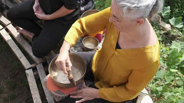 Top view of a mature woman playing a Tibetan singing bowl to induce meditation.