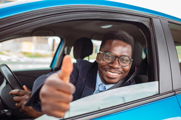 Happy african man show thumbs up inside car. Man at the wheel of his new car, showing thumb up. Young Smiling African American Male Thumb up in a Car
