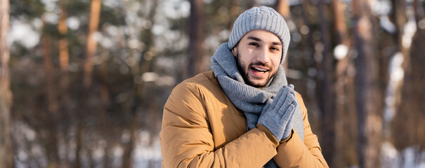 Positive man in warm clothes looking at camera in winter park, banner
