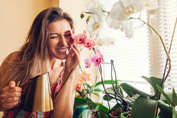 Happy woman touching orchids on window sill. Girl gardener taking care of home plants and flowers...