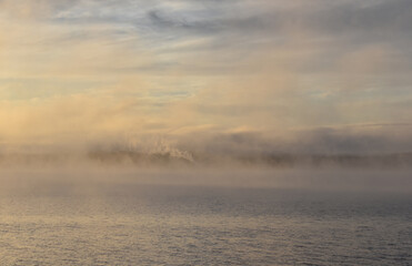 Steam rises from a factory at L'Anse Michigan across an early morning misty Keweenaw Bay from Baraga Michigan