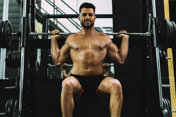 Obraz na płótnie Canvas Portrait of a strongman squatting with weights in a gym
