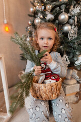 Beautiful little girl child in fashionable pajamas with a branch of christmas tree