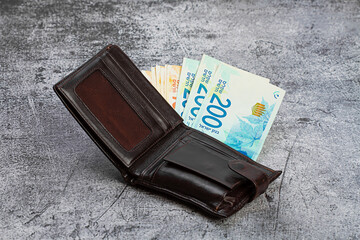 200 and 100 Israeli shekels banknotes stick out of a leather wallet.