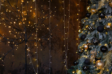 Beautiful festive Christmas tree in the room decorated with black and gold Christmas toys balls and wall with lights