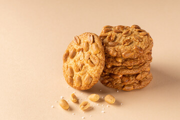 Stack of crunchy cookies with roasted peanuts on top on beige background. Front view. Place for text.